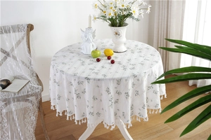 Close-up of white floral cotton tablecloth with fringe edges and small green patterns