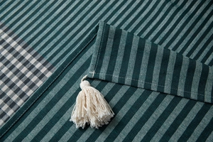 Detailed view of dark green striped tablecloth with woven texture and white cotton tassel