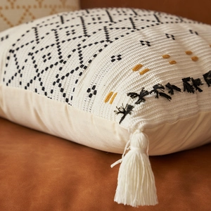 Dettaglio della federa per cuscino in maglia bohémien con motivi geometrici e nappe di cotone