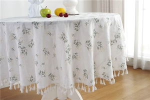 Close-up of white cotton floral tablecloth featuring green daisy patterns and white fringe