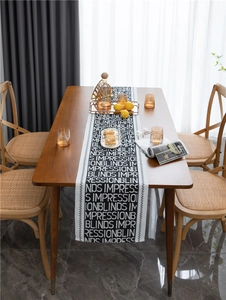 Detail of black woven table runner with white letter pattern on a wooden dining table