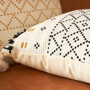 Dettaglio copricuscino lavorato a maglia boho con motivi geometrici e nappe bicolore