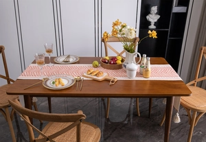 Close-up of bohemian table runner with orange wave pattern and white tassels on wood table