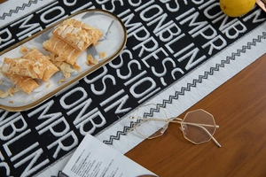 Detail of black and white jacquard table runner with letter patterns and wavy edges