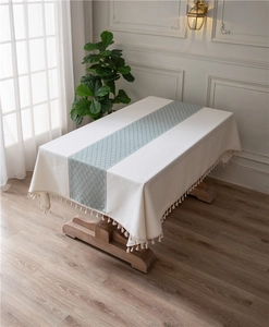 Close-up of beige rectangular tablecloth with green geometric pattern and tassel fringe