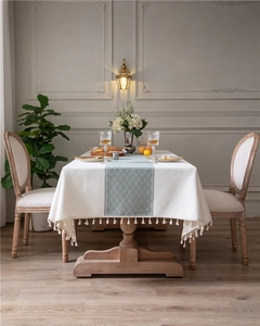 Detail of jacquard geometric table cloth with beige fabric, green patterns and tassel fringe