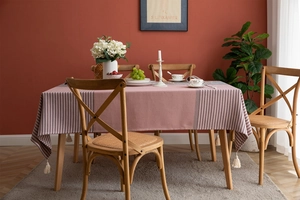Close-up of pink striped jacquard tablecloth with white tassels on a rustic wooden table