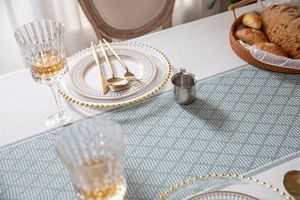 Detail of mint green geometric jacquard table runner with fringe on a white tablecloth