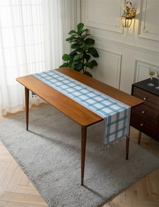 Detail of blue geometric checkered table runner with decorative tassel on wooden table