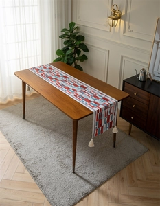 Detail of colorful geometric letter jacquard table runner with thick beige tassel accents
