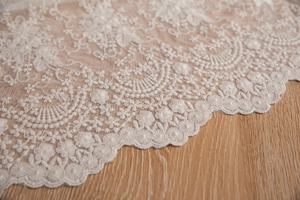 Détail d'une nappe en dentelle florale blanche avec bords festonnés sur fond de bois clair