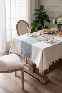 Detailed close-up of cream tablecloth with light blue geometric pattern and tassel fringe