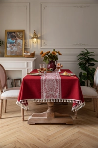 Detalle de mantel de jacquard rojo oscuro con borde de borlas blancas y patrón damasco