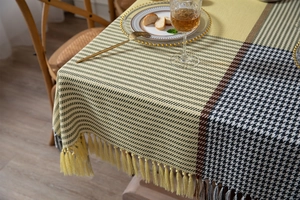 Detail view of yellow houndstooth tablecloth with decorative fringe on a wooden table