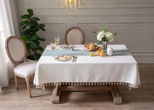 Detail of light green plaid table runner with white fringe tassels on linen tablecloth