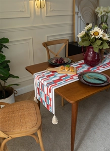 Detail of red and blue geometric jacquard table runner with white cotton tassels on wood table