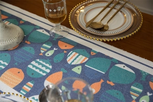 Détail d'un chemin de table à motif de poissons avec pompons sur une table en bois