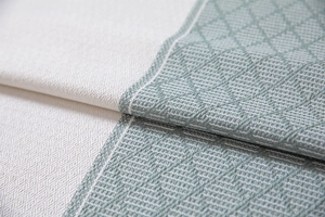 Detail of sage green geometric diamond weave pattern and cream white fabric fringe