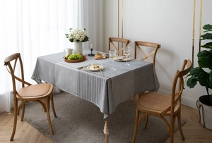 Close-up of modern gray and white striped tablecloth featuring corner tassels on a wooden table