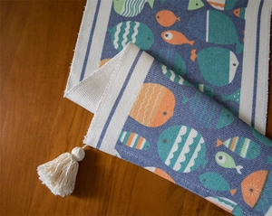 Détail du chemin de table tissé avec motifs poissons bleus et pompons en coton doux