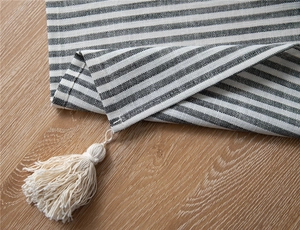 Detail of black and white striped tablecloth with tassels on a wooden surface