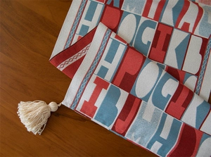 Close-up of jacquard table runner with red and blue letters and white fringe tassels