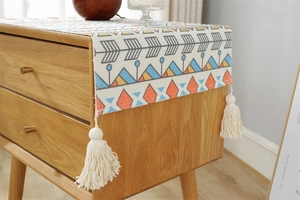 Detail of bohemian geometric print dust cover with white tassels on a wooden nightstand