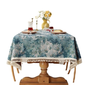 Blue jacquard floral tablecloth with fringes on round wooden table with vase
