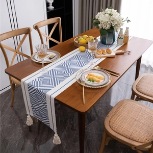 Blue and white geometric table runner with cream tassels on a dark wood dining table