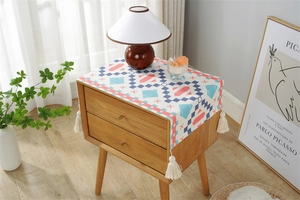 Detailed close-up of geometric printed dust cover with white tassels on a wooden cabinet