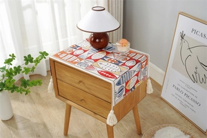 Detail of colorful abstract fish pattern table runner with creamy white tassels on wood