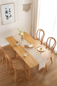 Close-up of white crochet lace table runner with wave edges and fringe on a wooden table