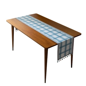 Modern blue and white plaid table runner with decorative tassel trim on wooden table