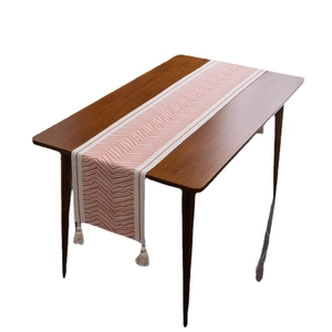Bohemian table runner with brick red wave patterns and cotton tassels on dark wood