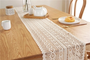 Detailed close-up of cream crochet lace table runner with floral hollow patterns on wood table