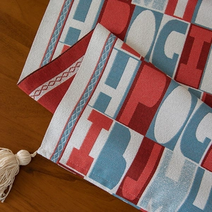 Red jacquard table runner with geometric letters and cream tassels on wood