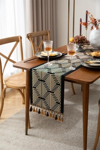 Close-up of geometric jacquard table runner with fringe tassels on a wooden dining table
