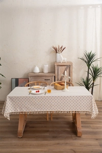Detail of beige tablecloth with blue floral print and decorative tassels on wood table