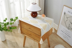 Close-up of woven dust cover with yellow leaf pattern and white cotton tassels on wood table