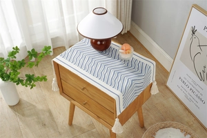 Detail of blue and white wave pattern table runner with creamy white tassels on wood cabinet