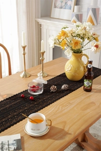 Close-up of black hollow lace table runner with floral crochet pattern on wooden table