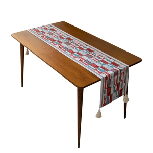 Modern table runner with red jacquard lettering and decorative tassels on wooden table