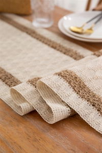 Close-up of bohemian linen table runner with woven tassels and diamond pattern on wood
