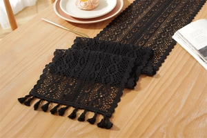 Close-up of black hollow lace table runner with elegant fringe trim on a wooden table