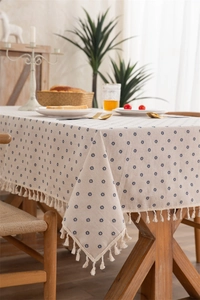 Detailed view of beige tablecloth with blue floral prints and elegant tassel edges