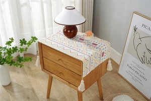 Close-up of geometric pattern dust cover with white tassels on a wooden bedside table