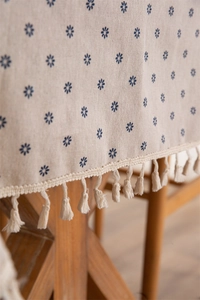 Close-up of beige cotton linen tablecloth with blue daisy prints and woven tassel fringe