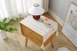 Macro detail of Bohemian geometric table runner with cotton tassels on wood nightstand