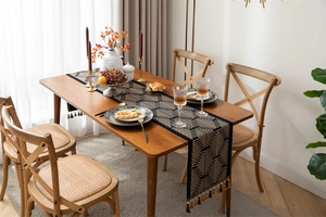 Detail of jacquard geometric table runner with multi-color tassels on a wooden dining table