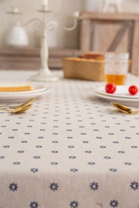 Close-up of beige cotton tablecloth with small blue daisy print and rustic fringe edge